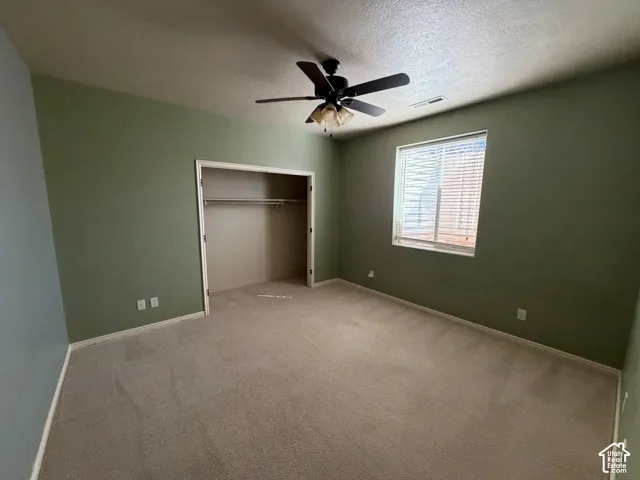 Carpeted interior space featuring a ceiling fan, a window with blinds, and a built-in closet with hanging rods
