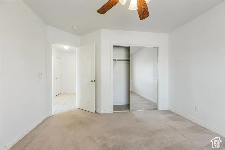 Carpeted room featuring a ceiling fan with light fixture, white walls, and a closet with mirrored sliding doors