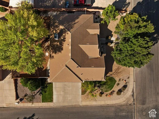 Warm-toned tile roofing, paved driveway, mature trees, and landscaped rock and grass accents