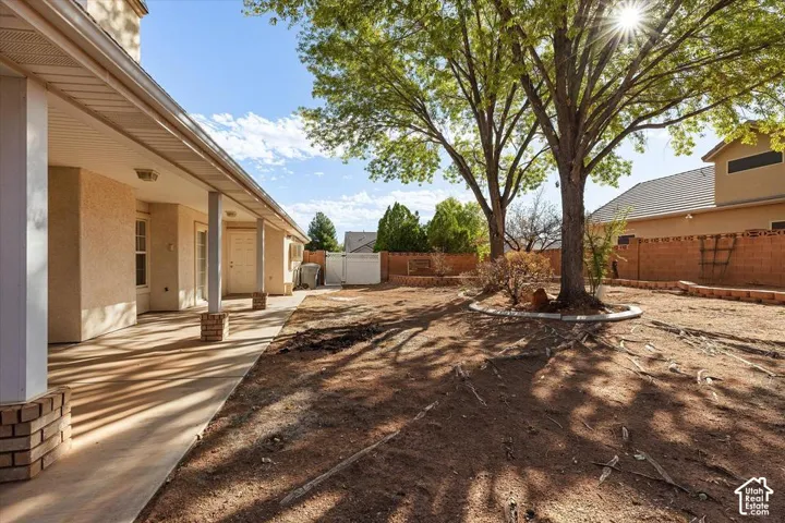 Covered concrete patio with brick-base columns, mature trees, and a block perimeter fence
