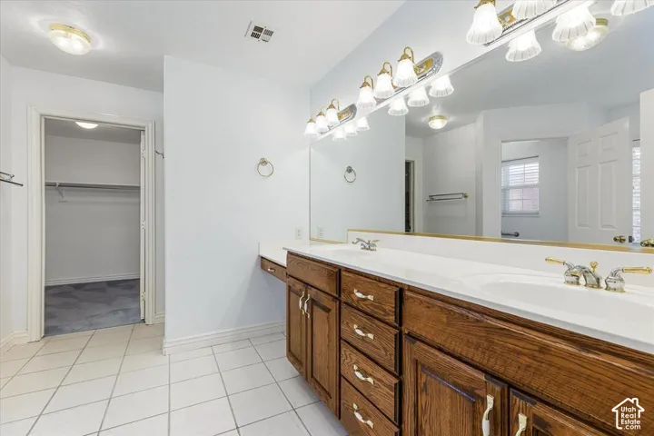Dual vanity with integrated sinks, wood-finish cabinetry, a full-width mirror, and tile flooring