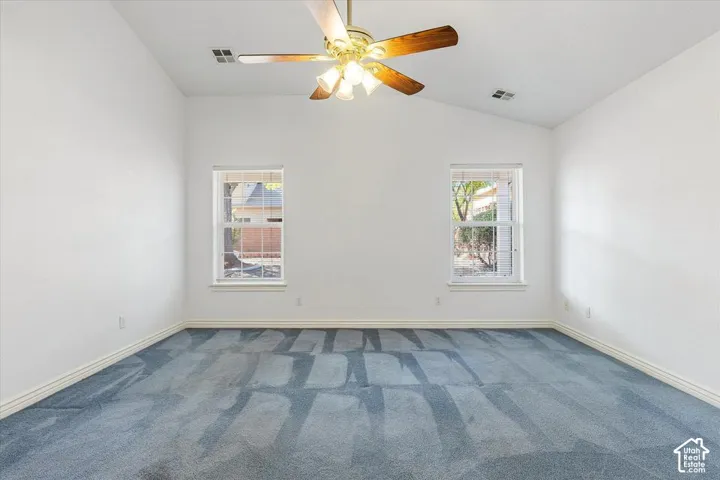 Vaulted ceiling with a ceiling fan, two windows, and blue carpet flooring
