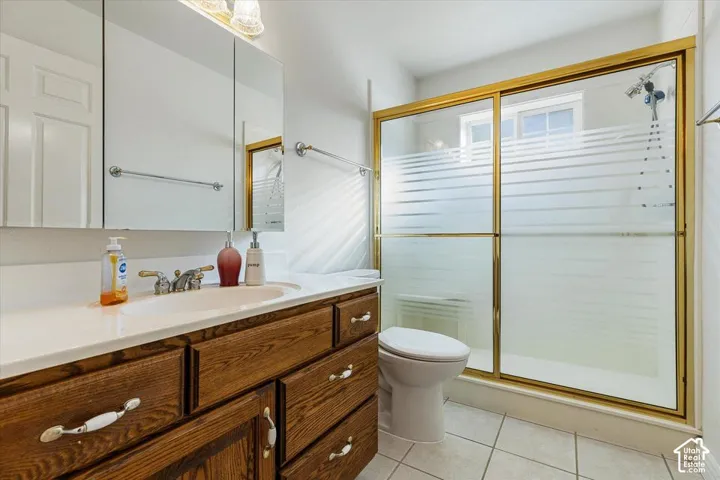 Wood-finish vanity with a single basin, white countertop, and gold-framed shower enclosure