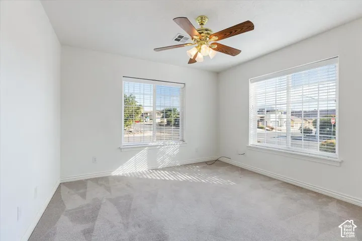 Recessed lighting, ceiling fan with light fixture, two windows with blinds, and light-colored carpeting