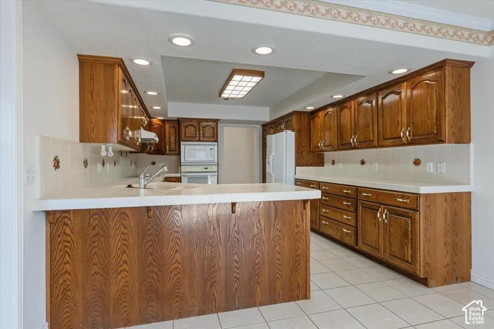 Kitchen featuring recessed lighting, a built-in microwave, wood cabinetry, tile flooring, and a white tile backsplash
