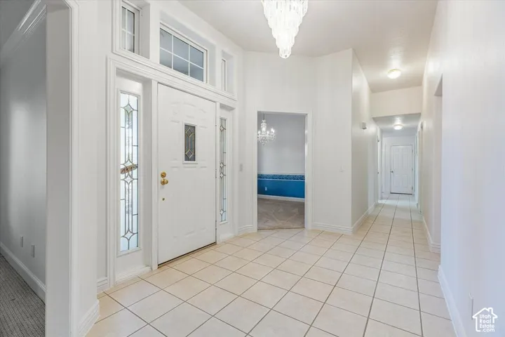 Tiled entryway featuring a decorative front door with sidelights and transom windows, a chandelier, and recessed lighting