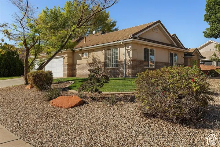 Tiled roofing, stucco exterior, brick wainscoting, mature landscaping, and an attached two-car garage