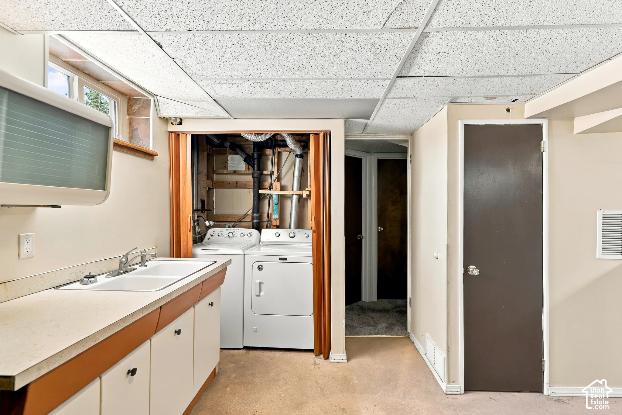 Laundry area featuring a double basin utility sink, white base cabinetry, and a drop ceiling