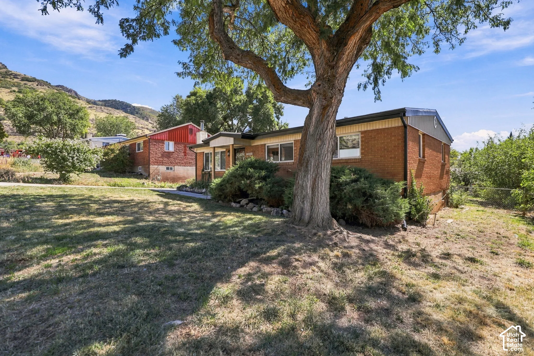 Brick exterior, mature front yard tree, established shrubbery, paved walkway, and a partial mountain backdrop