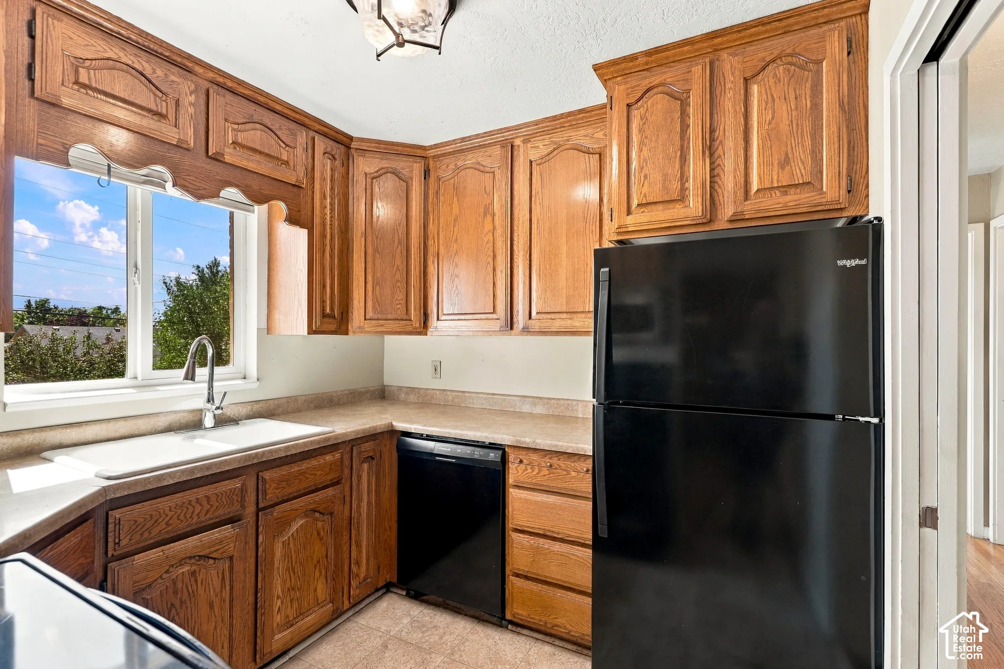 Kitchen with wood cabinetry, light-toned countertops, a stainless steel sink, and a black refrigerator
