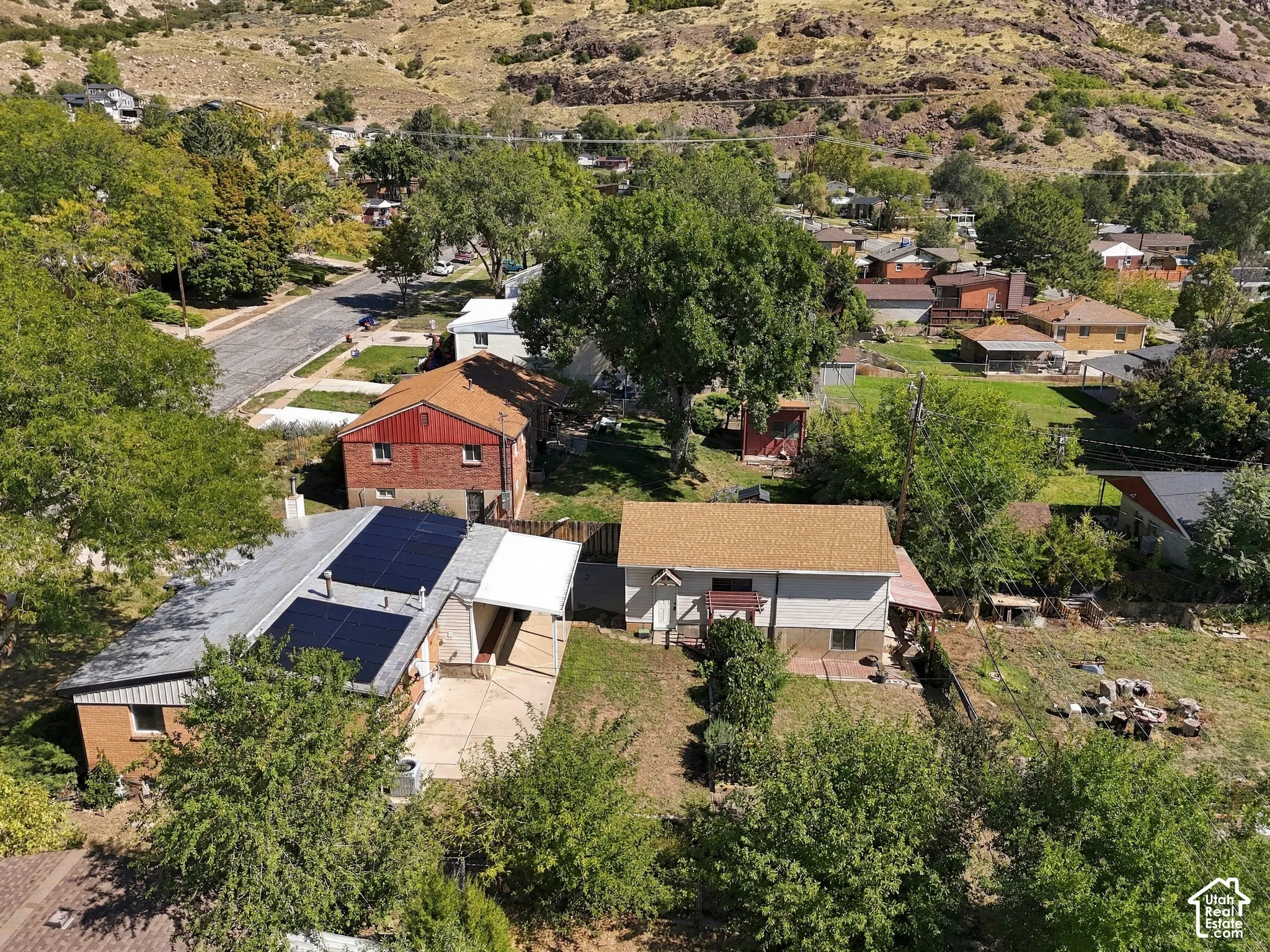 Rooftop solar panels, rear patio, sloped hillside, surrounding mature trees, and mountainous backdrop