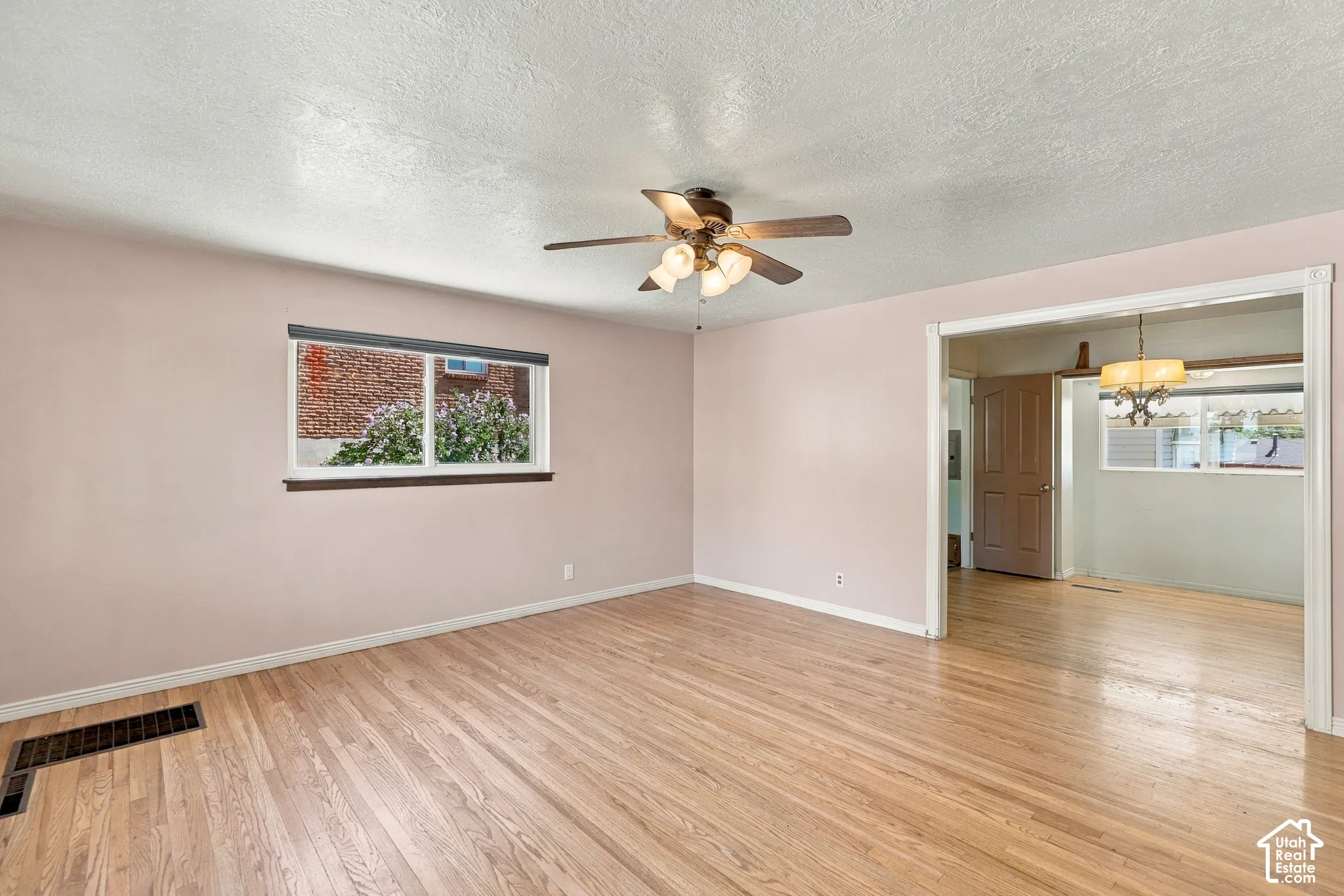 Natural wood-finish flooring with a ceiling fan light fixture and a window with blinds