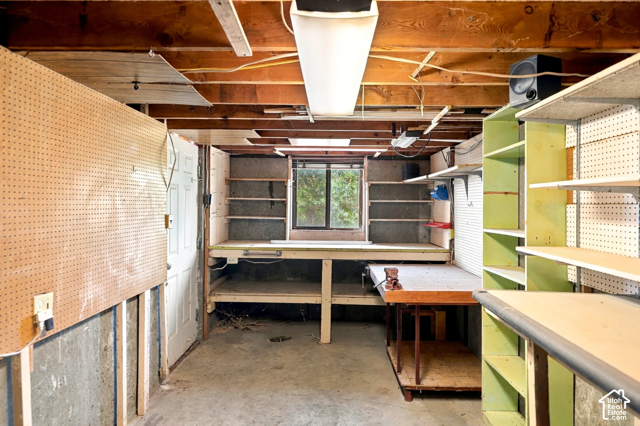 Concrete flooring, pegboard wall panels, built-in shelving, exposed ceiling joists, and a casement window