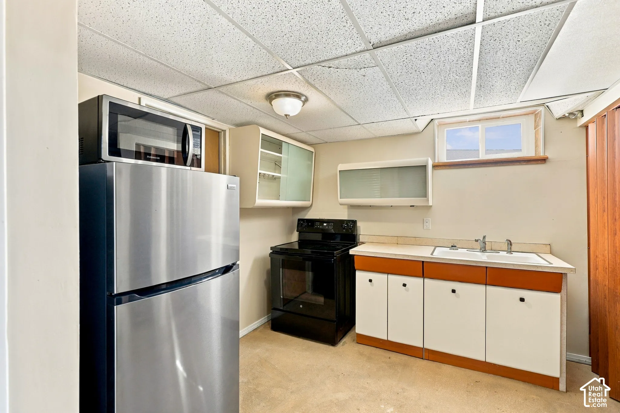 Stainless steel refrigerator and microwave, black electric range, white cabinetry with wood-finish trim, and drop ceiling