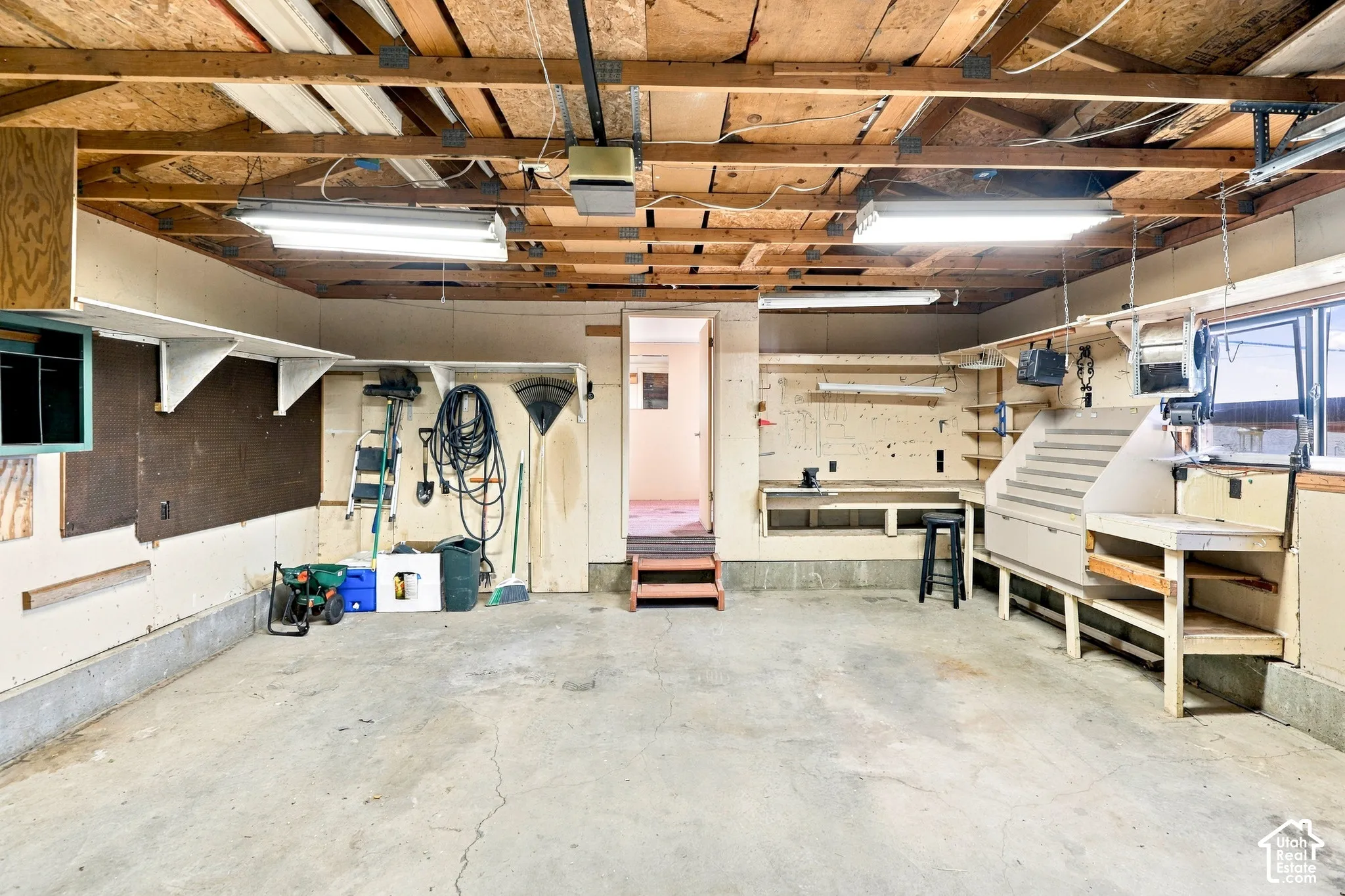Concrete flooring with exposed wood beam ceiling, featuring built-in shelving, a workbench, and a window