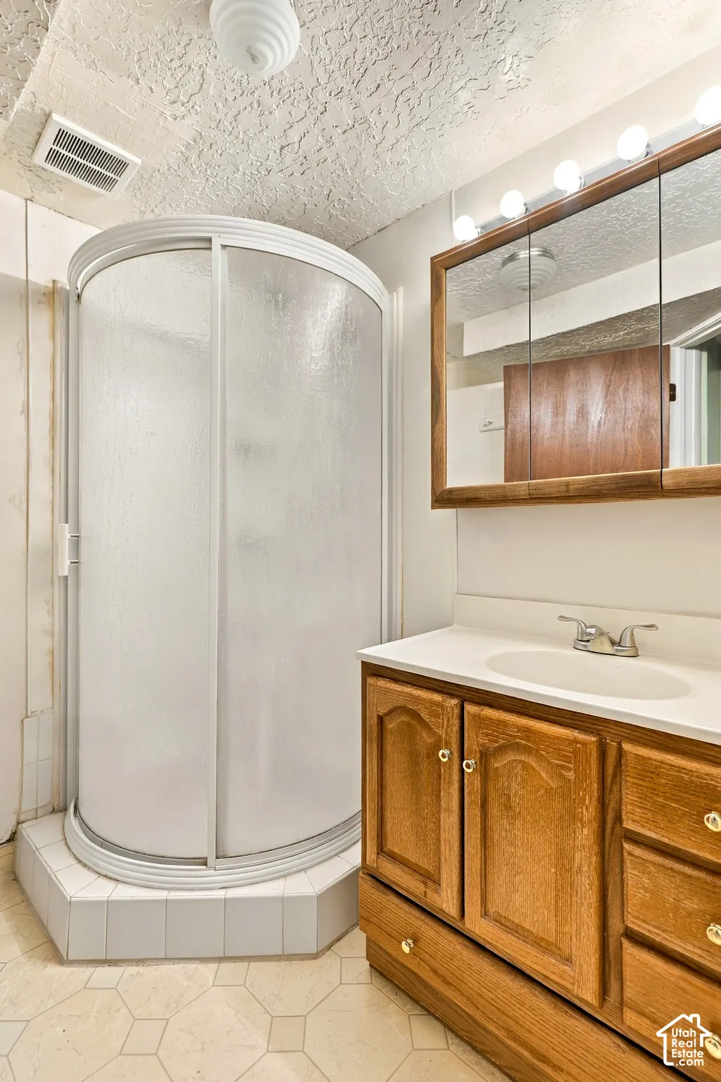 Corner shower enclosure with sliding frosted glass doors, a vanity with a white countertop and integrated sink, a wood-finish medicine cabinet with integrated lighting, and an overhead light fixture