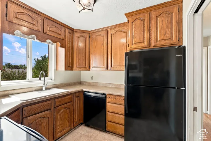 Kitchen with wood cabinetry, light-toned countertops, a stainless steel sink, and a black refrigerator