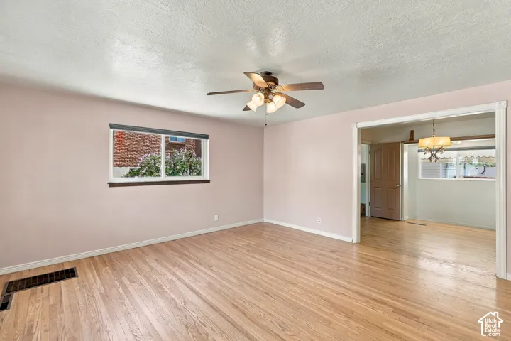 Natural wood-finish flooring with a ceiling fan light fixture and a window with blinds