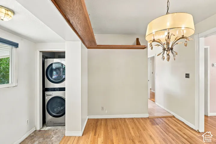 Hardwood flooring, exposed wood beam, stacked laundry appliances, chandelier light fixture, and a window with a roller shade