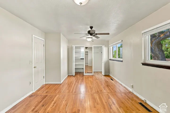 Hardwood flooring, two windows, ceiling fan with integrated lighting, and a built-in closet with shelving and mirror