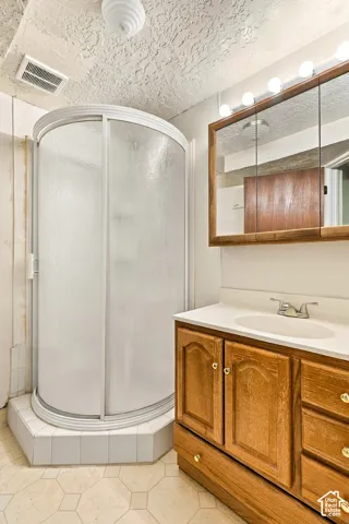 Corner shower enclosure with sliding frosted glass doors, a vanity with a white countertop and integrated sink, a wood-finish medicine cabinet with integrated lighting, and an overhead light fixture