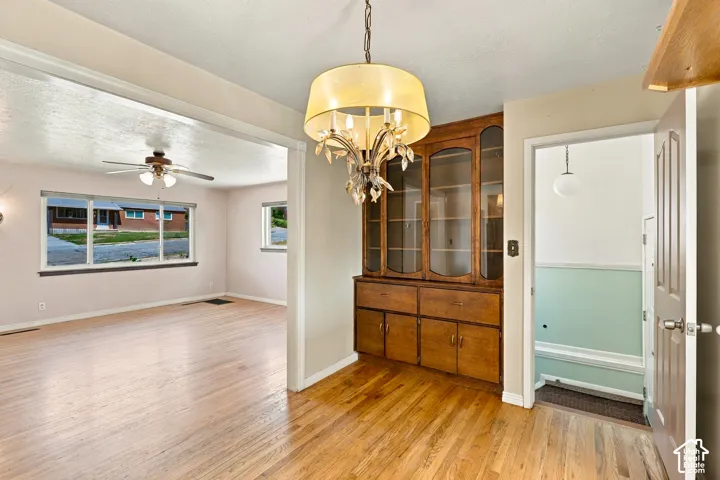 Hardwood flooring, built-in display cabinetry, ceiling fan with integrated lighting, and a decorative chandelier