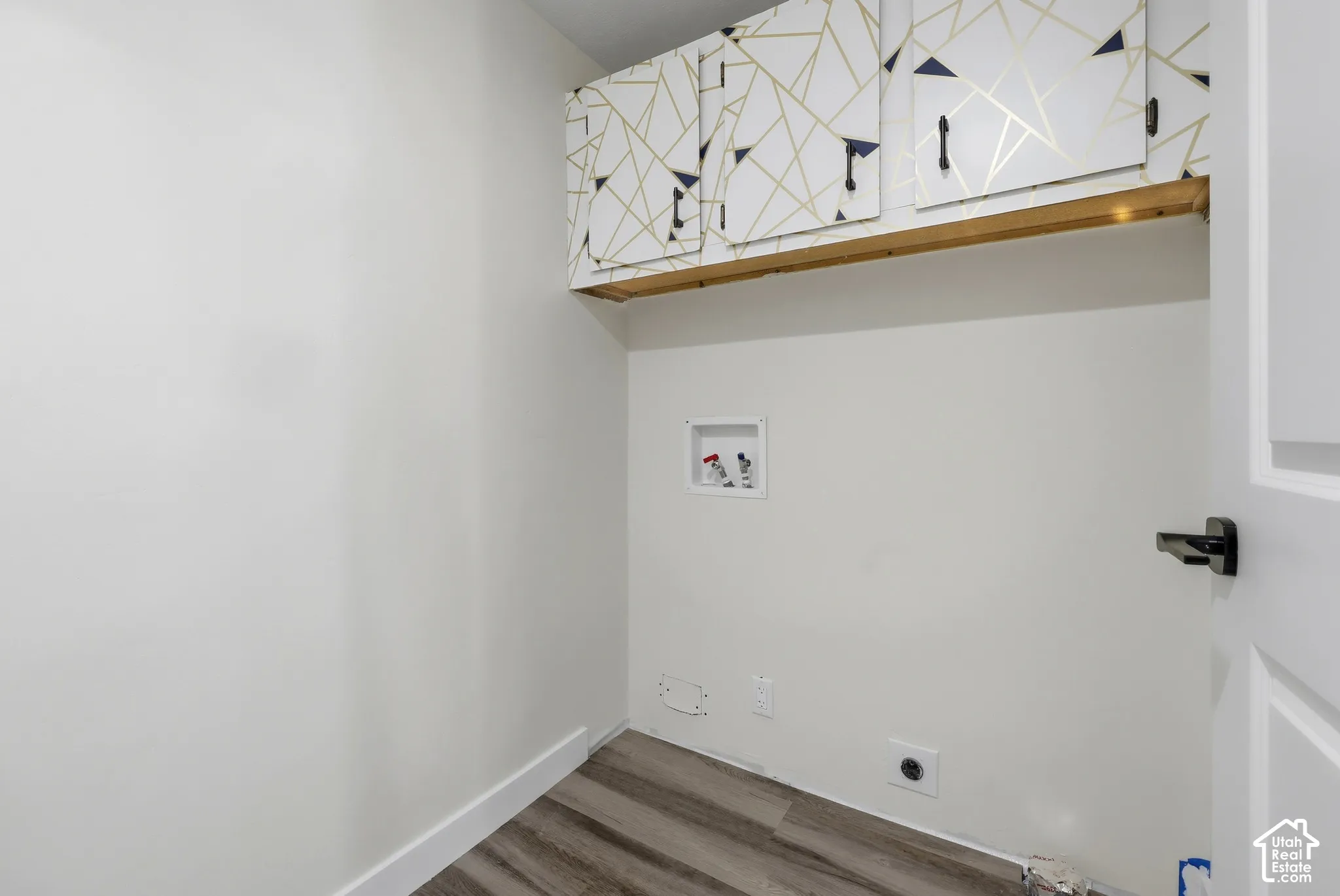 Wood-finish flooring with white baseboards, white walls, and built-in patterned overhead cabinetry with a wood shelf
