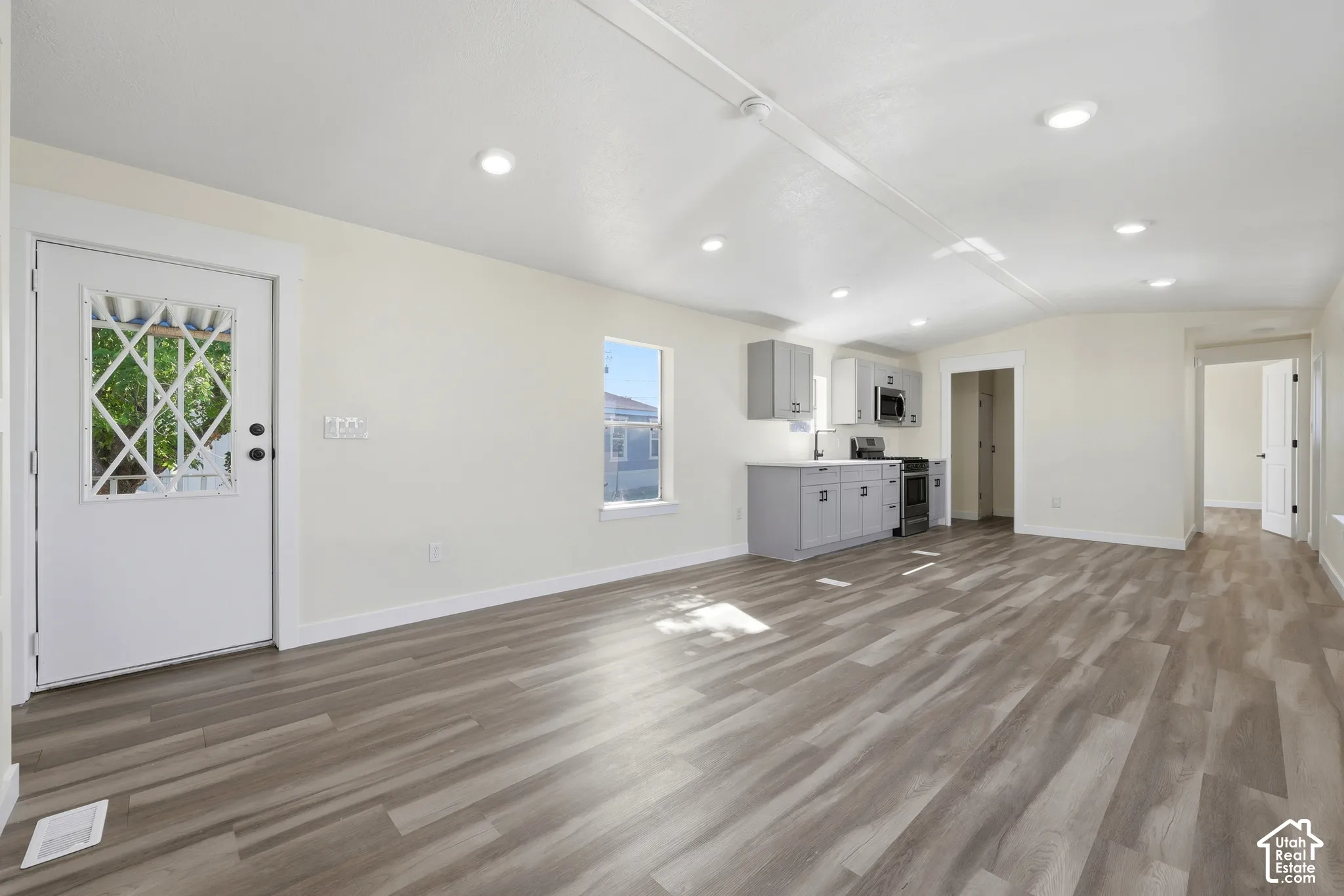 Wood-finish flooring, recessed lighting, white walls, gray cabinetry, and a white entry door with decorative glass