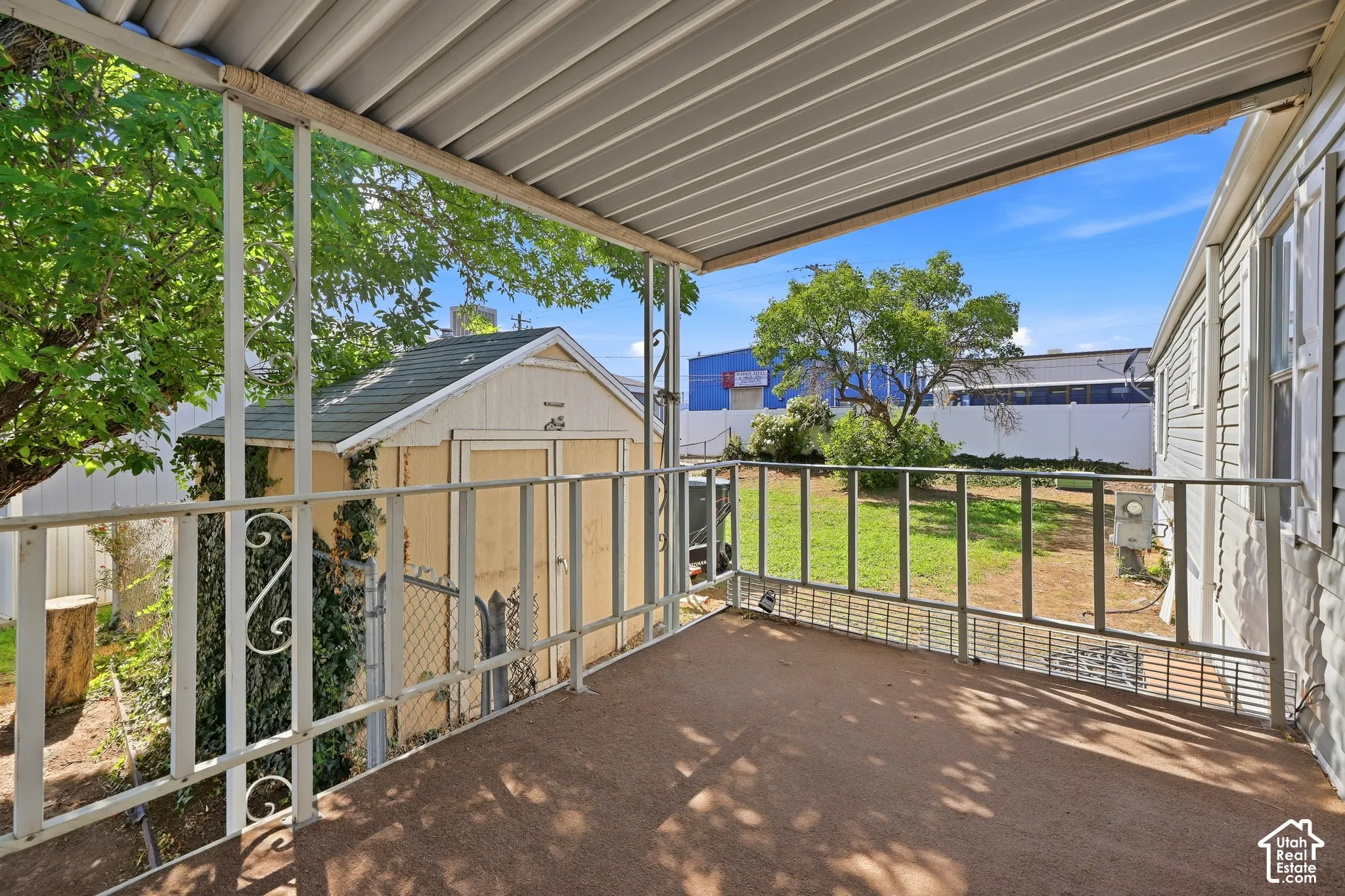 Covered patio with metal railing and textured flooring, overlooking a grass yard and detached storage shed
