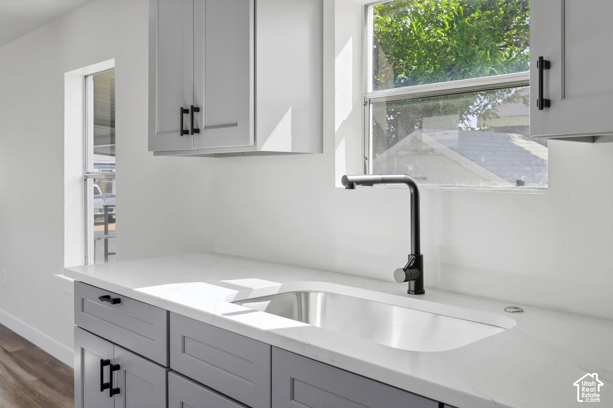 White countertops with an integrated sink, matte black faucet, and gray cabinetry