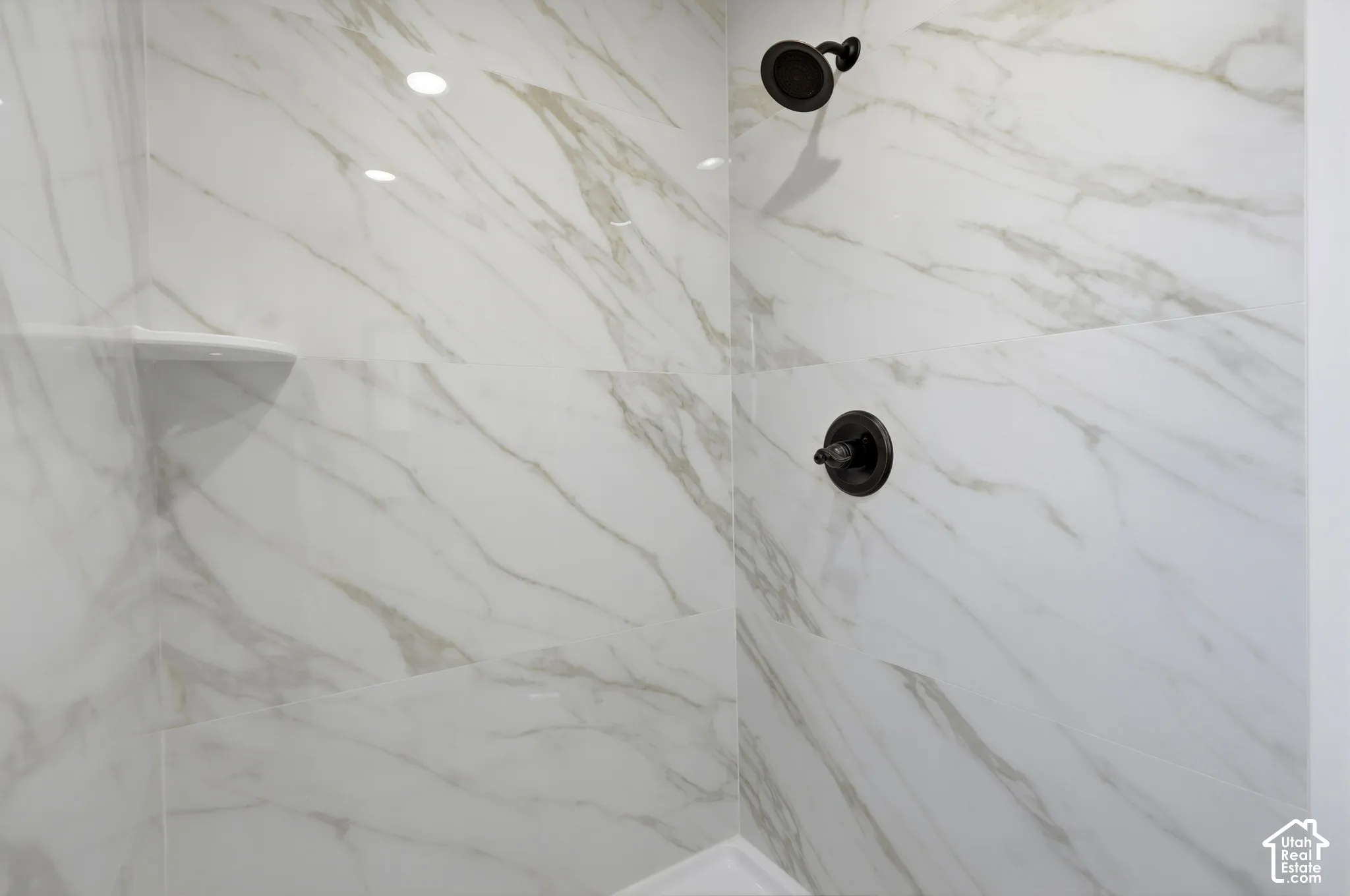 Shower featuring white marble-look wall tiling, a built-in shelf, and dark bronze fixtures