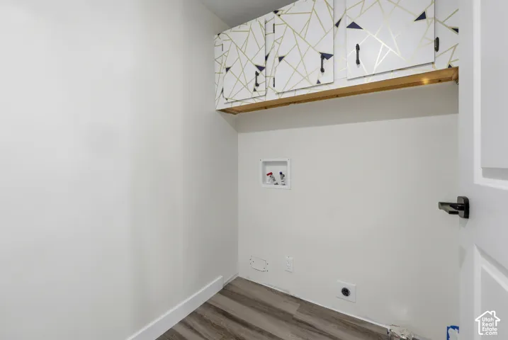 Wood-finish flooring with white baseboards, white walls, and built-in patterned overhead cabinetry with a wood shelf