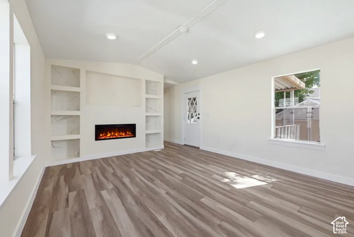 Recessed electric fireplace with built-in shelving, wood-finish flooring, white paneled door with decorative glass, and recessed lighting