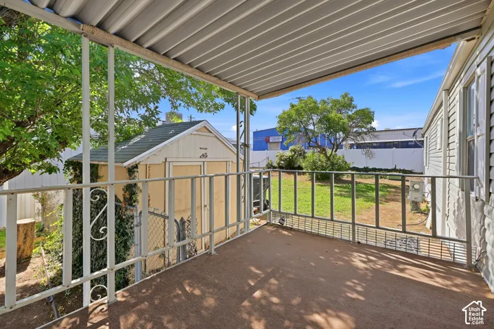 Covered patio with metal railing and textured flooring, overlooking a grass yard and detached storage shed