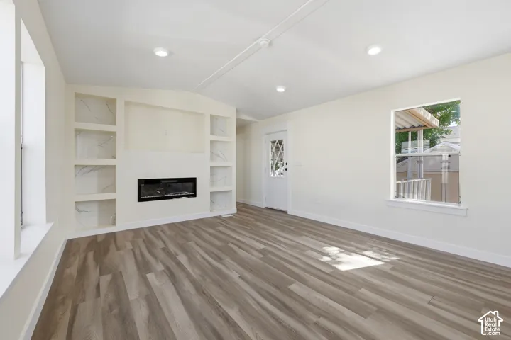 Built-in shelving with decorative backing, electric fireplace, wood-finish flooring, recessed lighting, and a paneled entry door with decorative glass