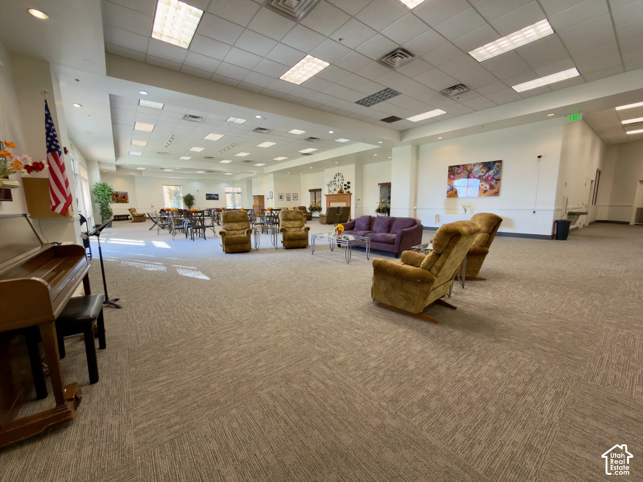 Expansive community room featuring patterned carpeting, recessed lighting, varied seating arrangements, and a built-in fireplace