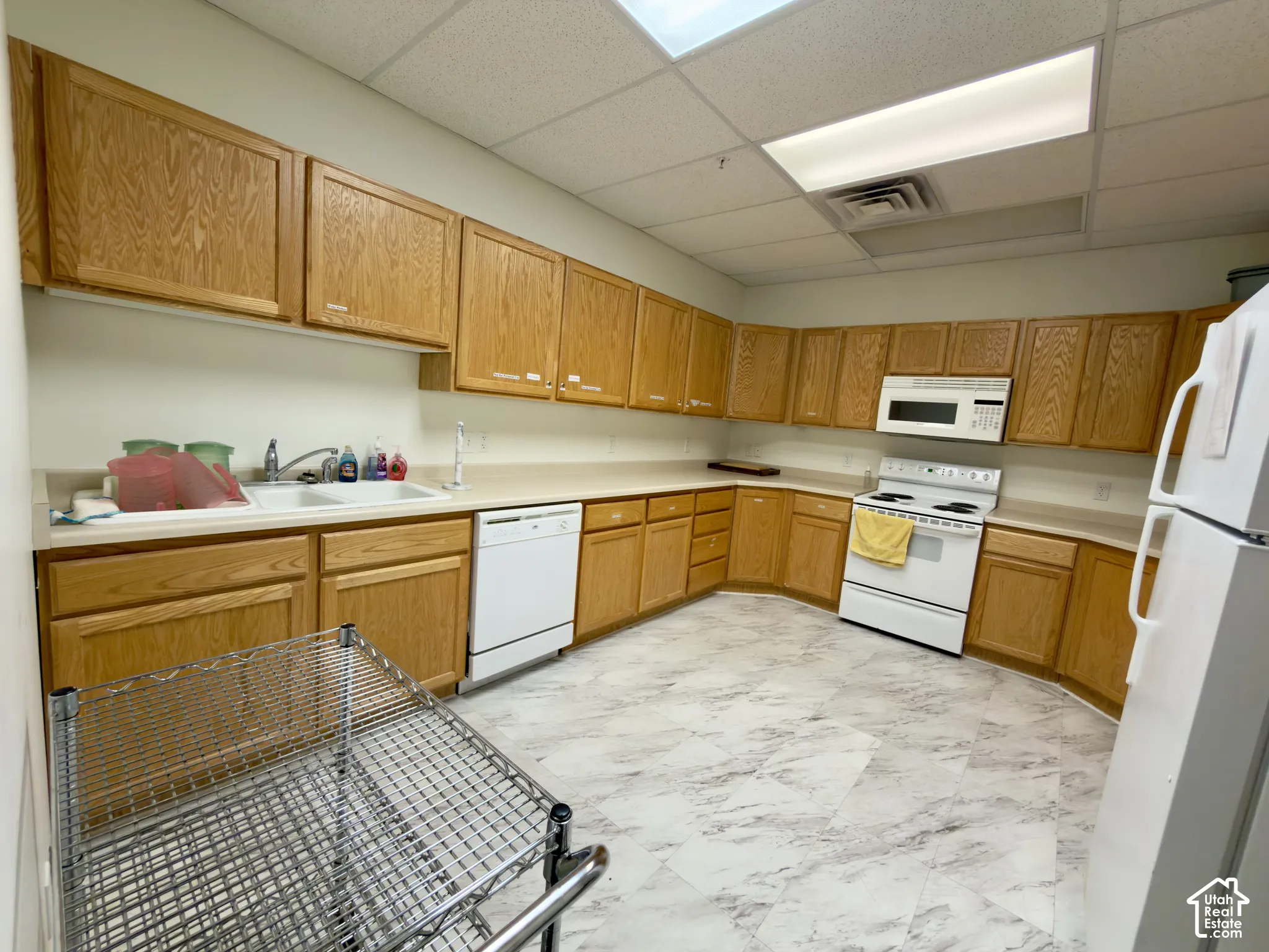 Spacious clubhouse kitchen featuring extensive wood cabinetry, white appliances, a double basin sink, and patterned flooring