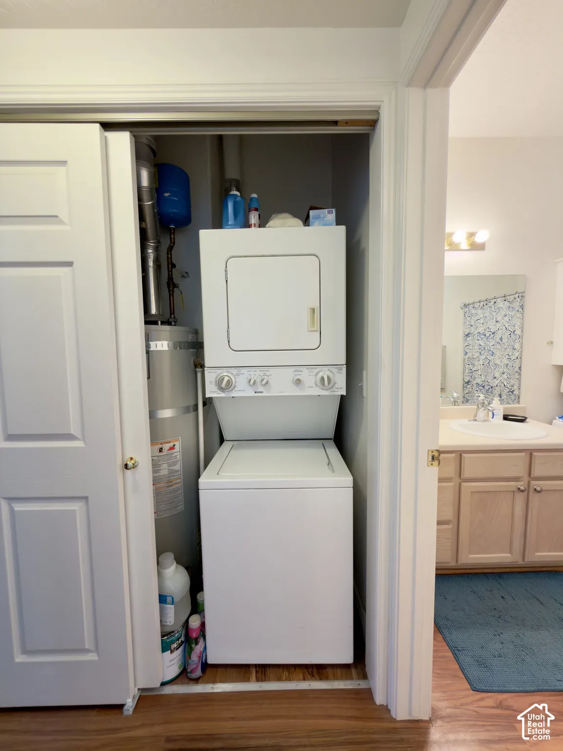 Integrated laundry closet featuring an included white stacked washer and dryer, adjacent to a bathroom with a wood-finish vanity
