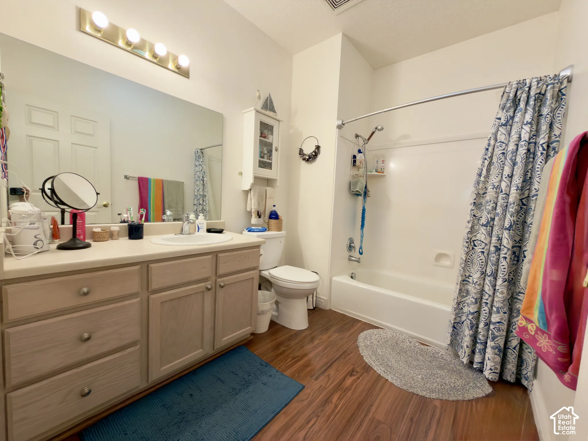 Large bathroom w/ vanity, full-width mirror, overhead light fixture, laminate flooring, and a bathtub with shower