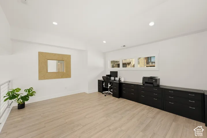 Recessed lighting, light wood-finish flooring, a series of horizontal windows, and a built-in black storage system with a dark countertop