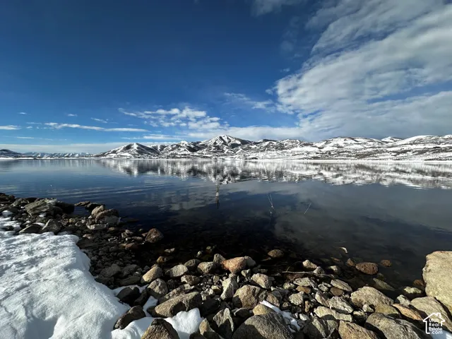 Expansive body of water with reflections, bordered by a rocky shoreline and snow-covered terrain
