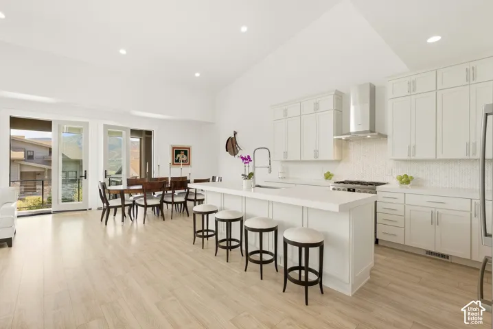 Vaulted ceiling open-concept kitchen and dining area featuring light wood-finish flooring, white cabinetry, a built-in kitchen island, and stainless steel appliances