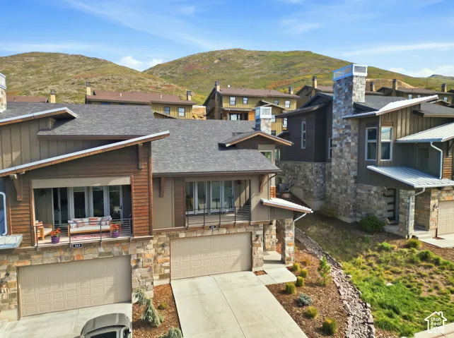 Multi-story residence featuring a stone and wood siding exterior, attached two-car garage, and a balcony with metal railings