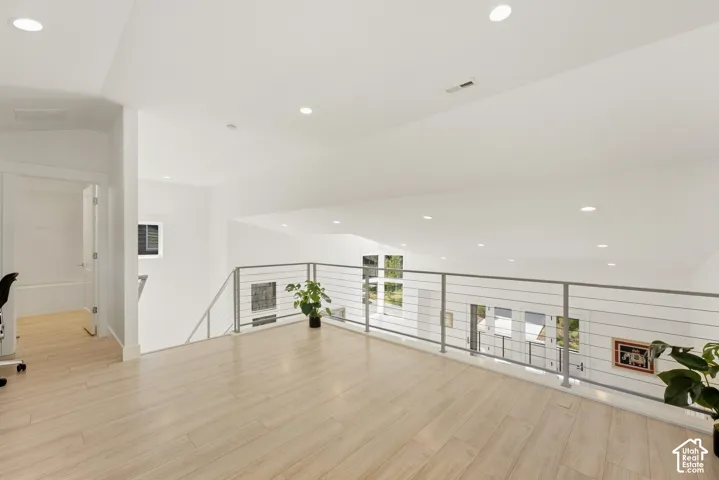 Open loft area featuring wood-finish flooring, recessed lighting, and a contemporary cable railing system