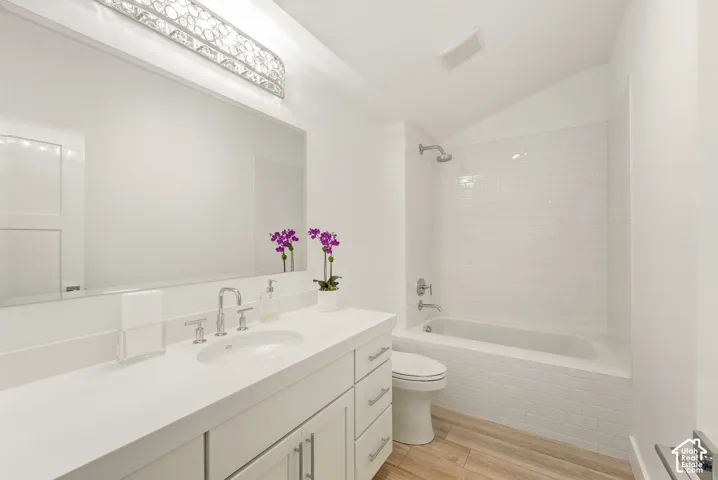 Vanity with a single basin sink and brushed nickel faucet, large wall-mounted mirror, decorative light fixture, white subway tile shower surround, and wood-finish flooring