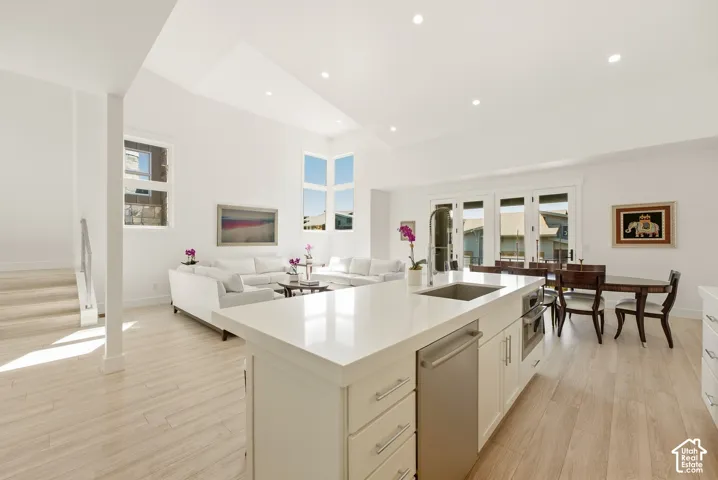 Open-concept living space featuring vaulted ceilings, recessed lighting, wood-finish flooring, a kitchen island with an undermount sink, and French doors