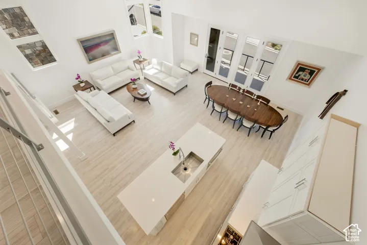 Open-concept living area with high ceilings, wood-finish flooring, a kitchen island with an integrated sink, and an expansive set of French doors