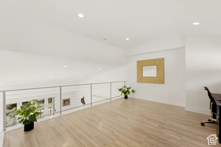 Spacious loft area featuring wood-finish flooring, recessed lighting, and a cable railing system