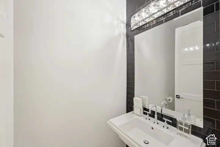 Pedestal sink with chrome faucet, large vanity mirror, and black subway tile accent wall