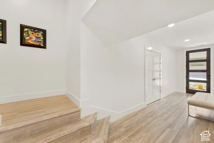 Light wood-finish flooring throughout, modern entry door with horizontal glass panels, white interior doors with frosted glass, recessed lighting, and crisp white walls